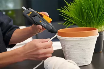 ein Blumentopf wird mithilfe von Heißkleber mit einer Kordel beklebt