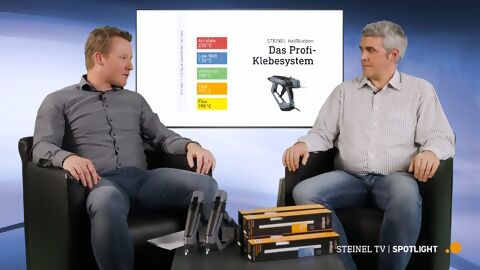 zwei Steinel-Mitarbeiter sitzen auf einem Sofa, vor Ihnen liegen unterschiedliche Klebestickverpackungen und Heißklebepistolen, über die sie sich unterhalten