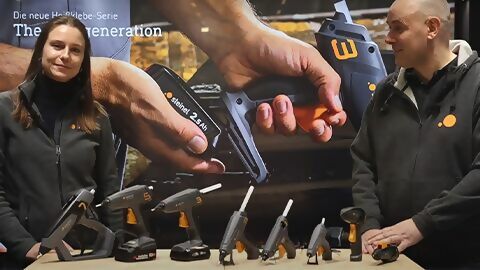 eine Mitarbeiterin und ein Mitarbeiter von STEINEL stehen vor einem Tisch, auf dem alle neuen Heißklebepistolen aufgereiht sind