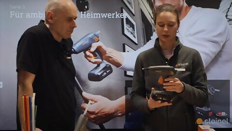 eine Mitarbeiterin und ein Mitarbeiter von STEINEL halten eine Heißklebepistole in der Hand und sprechen über diese
