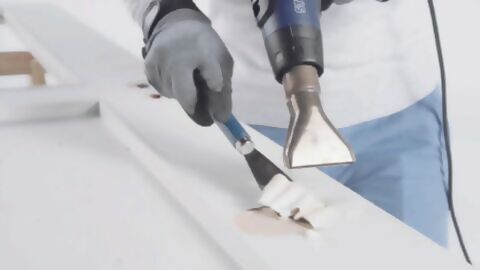 mithilfe eines Heißluftgerätes und einem Spachtel wird alte Farbe von einer Holztür entfernt