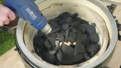 Ein Grill mit Holzkohle wird mithilfe eines Heißluftgerätes erhitzt