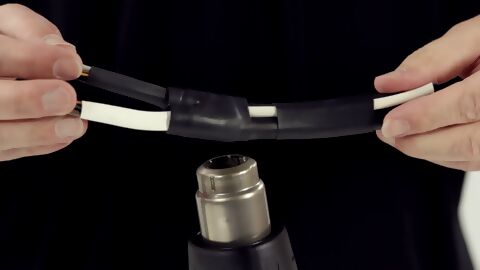 zwei dicke Kabel werden mithilfe einen Heißluftgebläses und aufgesteckter Reflektordüse geschrumpft