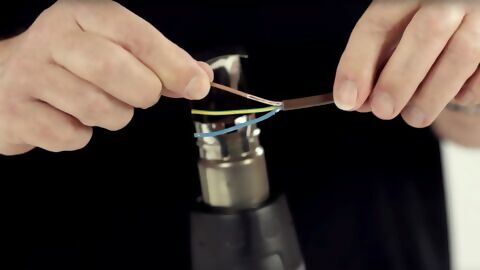 drei Kabel werden mithilfe eines Heißluftgebläses und aufgesteckter Reflektordüse mit einem Schrumpfschlauch gebündelt