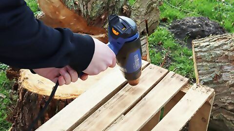 Eine Holzkiste wird mithilfe eines Heißluftgerätes abgeflämmt